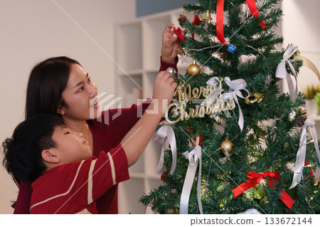 SSTK Christmas. Mother and son decorating a Christmas tree together with ornaments and ribbons. 133672144