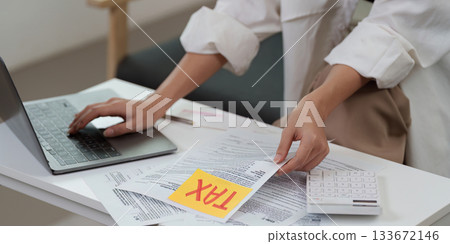 Tax preparation. Individual organizing tax documents and using calculator for financial planning. 133672146