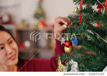 SSTK Christmas. Woman carefully hanging a shiny ornament on a beautifully decorated Christmas tree. SSTK Christmas. Woman carefully hanging a shiny ornament on a beautifully decorated Christmas tree. 133672187