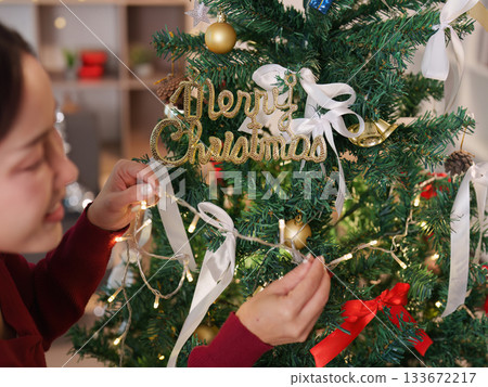 SSTK Christmas: Woman adding lights and ribbons to a beautifully decorated tree SSTK Christmas: Woman adding lights and ribbons to a beautifully decorated tree 133672217