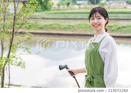 An Asian woman wearing an apron watering the garden trees in her home 133672260