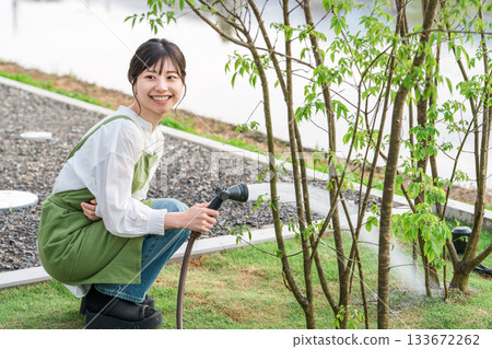 一位身穿圍裙的亞洲婦女正在自家花園澆水。 133672262