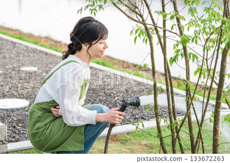 一位身穿圍裙的亞洲婦女正在自家花園澆水。 133672263