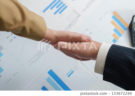 Handshake Agreement. Business professionals sealing a deal with a handshake over financial charts. Handshake Agreement. Business professionals sealing a deal with a handshake over financial charts. 133672294
