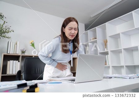Health and Wellness. Woman experiencing discomfort while working on a laptop in an office. Health and Wellness. Woman experiencing discomfort while working on a laptop in an office. 133672332