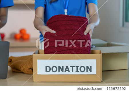 Donation Activity. Volunteer placing a sweater into a donation box. 133672392