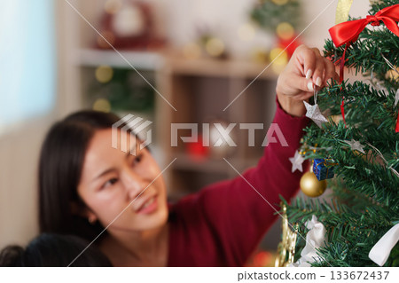 SSTK Christmas: Woman carefully hanging ornaments on the Christmas tree SSTK Christmas: Woman carefully hanging ornaments on the Christmas tree 133672437