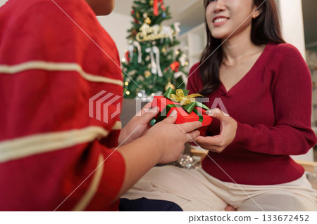 SSTK Christmas. A joyful moment of a child giving a gift to a woman by the Christmas tree. SSTK Christmas. A joyful moment of a child giving a gift to a woman by the Christmas tree. 133672452