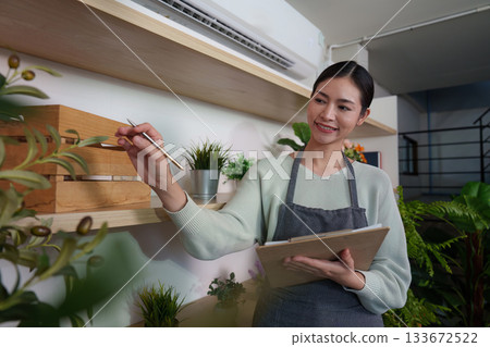Plant Care. Woman smiling while recording details in a plant shop, promoting sustainability. Plant Care. Woman smiling while recording details in a plant shop, promoting sustainability. 133672522