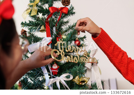 Christmas Tree Ornamenting. Close-up of hands adding decorations to a tree. Christmas Tree Ornamenting. Close-up of hands adding decorations to a tree. 133672616