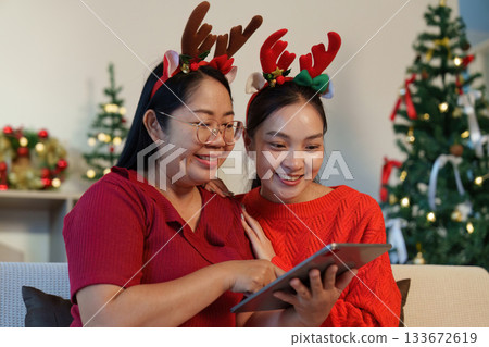 Holiday Joy. Two women enjoying festive moments with a tablet at home. Holiday Joy. Two women enjoying festive moments with a tablet at home. 133672619