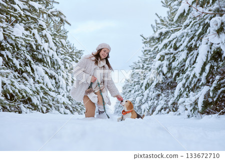 girl in winter clothes plays with Beagle dog in winter in the snow, winter holiday concept. 133672710