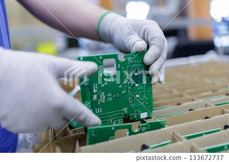 Worker in protective gloves placing green printed circuit board into cardboard tray for safe storage and shipping in electronics plant Worker in protective gloves placing green printed circuit board into cardboard tray for safe storage and shipping in electronics plant 133672737