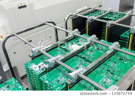 Stacks of green printed circuit boards stored in metal racks inside modern automated electronics manufacturing plant Stacks of green printed circuit boards stored in metal racks inside modern automated electronics manufacturing plant 133672739