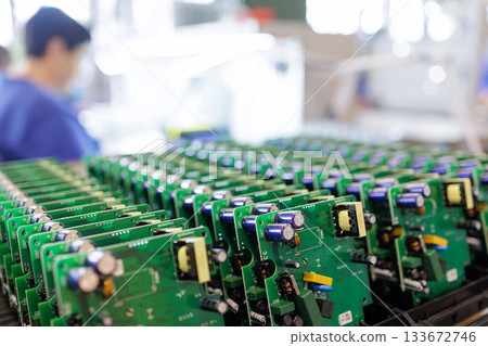 Rows of assembled green printed circuit boards in racks with factory worker in background at modern electronics production line Rows of assembled green printed circuit boards in racks with factory worker in background at modern electronics production line 133672746