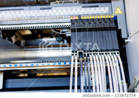 Close view of surface mount pick and place machine with electronic component tape feeders in modern automated assembly plant Close view of surface mount pick and place machine with electronic component tape feeders in modern automated assembly plant 133672754