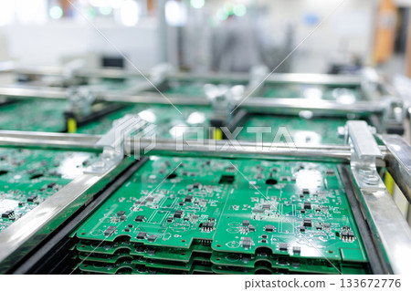 Stacks of assembled green printed circuit boards in metal rack on cart inside smart automated electronics factory 133672776