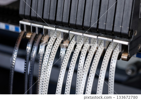 Closeup of SMT component feeder with reels of microelectronic parts used for automated PCB assembly in high tech manufacturing plant 133672780