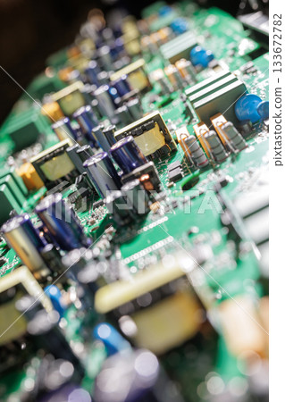 Closeup of green electronic circuit board with capacitors transformers and other power components under bright workshop light 133672782