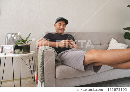Man relaxing on couch using smartphone at home 133673103