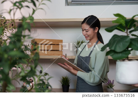 Sustainable Lifestyle. Woman enjoying plant care while taking notes in a shop setting. 133673516