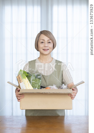 A senior woman rejoices in the delivery of vegetables delivered directly from the farm in her living room 133673929