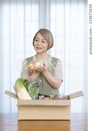 A senior woman rejoices in the delivery of vegetables delivered directly from the farm in her living room 133673939