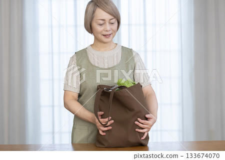 Senior woman taking vegetables out of a shopping bag in the living room 133674070