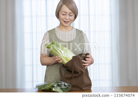 一位老婦人在客廳從購物袋裡拿出蔬菜 133674074