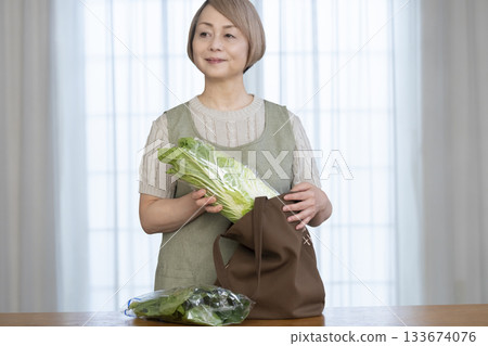 一位老婦人在客廳從購物袋裡拿出蔬菜 一位老婦人在客廳從購物袋裡拿出蔬菜 133674076