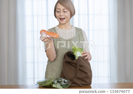 一位老婦人在客廳從購物袋裡拿出蔬菜 一位老婦人在客廳從購物袋裡拿出蔬菜 133674077