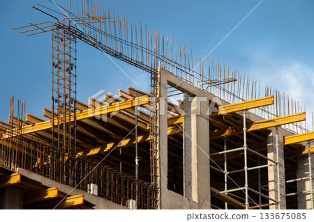 Monolithic Box under Construction with Yellow Volumetric I-Beams. Concrete Wall Frame Building with Formwork Prints and Rebar releases on Construction Site. Architectural origin Structure Sunny day. Monolithic Box under Construction with Yellow Volumetric I-Beams. Concrete Wall Frame Building with Formwork Prints and Rebar releases on Construction Site. Architectural origin Structure Sunny day. 133675085