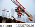 Close-up of Control Cabin of Red Tower Crane with Counterweight at Construction Site. In Foreground are Yellow Formwork Beams with Monolithic Box Fittings. 133675086