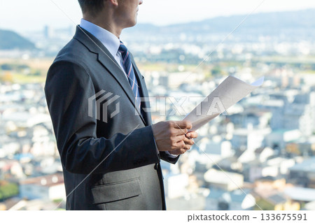 A middle-aged male businessman looking at a cityscape and real estate drawings 133675591