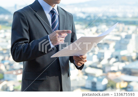 A middle-aged male businessman looking at a cityscape and real estate drawings A middle-aged male businessman looking at a cityscape and real estate drawings 133675593
