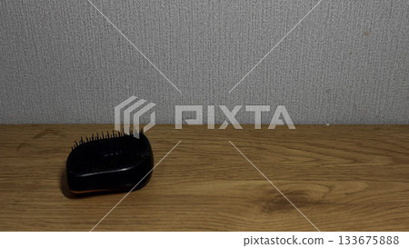 Elegant black hairbrush resting on a wooden table. Elegant black hairbrush resting on a wooden table. 133675888