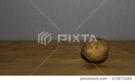 A single potato resting on a wooden surface. 133675889