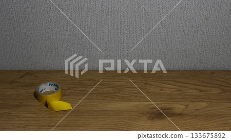 A close-up of a yellow tape roll on a wooden table. 133675892