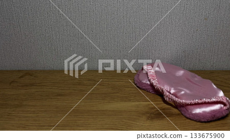 A soft pink sleep mask resting on a wooden table. A soft pink sleep mask resting on a wooden table. 133675900