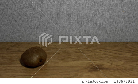 A single kiwi fruit on a wooden surface with a gray wall. A single kiwi fruit on a wooden surface with a gray wall. 133675931
