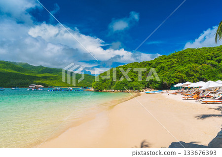 summer landscape with a white sandy beach with sun loungers and umbrellas in an azure bay by the sea on a sunny day at resort on a paradise island 133676393