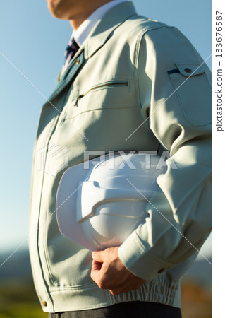 A middle-aged male businessman wearing work clothes and holding a helmet A middle-aged male businessman wearing work clothes and holding a helmet 133676587