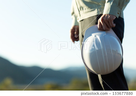 A middle-aged male businessman wearing work clothes and holding a helmet 133677880