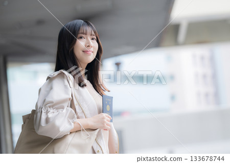 一位面帶微笑的年輕女子手持護照，準備出國旅行，場景即將開始。 133678744