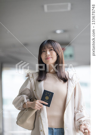 Smiling young woman holding a passport for overseas travel and departure scene Smiling young woman holding a passport for overseas travel and departure scene 133678748