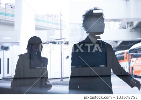 Silhouettes of men and women walking through a station or airport (terminal)-like place reflected through glass, and urban transit scenery Silhouettes of men and women walking through a station or airport (terminal)-like place reflected through glass, and urban transit scenery 133678753