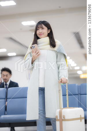 冬季,一位年輕女子在機場大廳裡,手裡拿著智慧型手機和行李箱,這是她旅行時的場景。 冬季,一位年輕女子在機場大廳裡,手裡拿著智慧型手機和行李箱,這是她旅行時的場景。 133679098