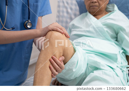 Doctor checking Asian elderly woman patient with scar knee replacement surgery in hospital. 133680662