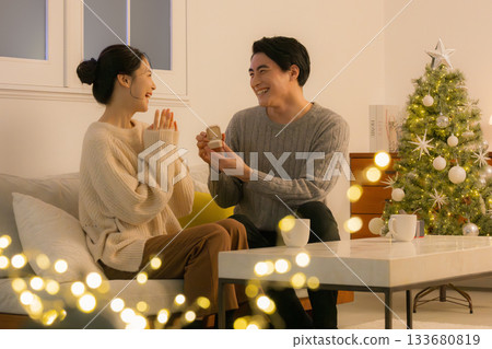 一位女士在聖誕樹前收到禮物時欣喜不已。這是一張展現冬季節慶氛圍的情侶互贈禮物的照片。 133680819