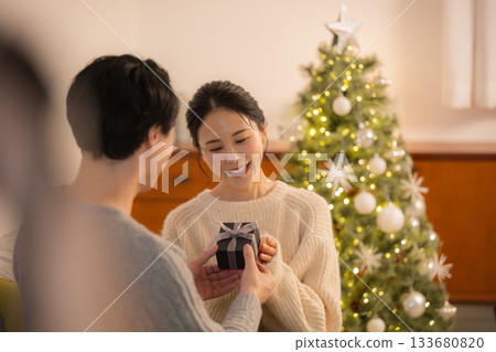 一位女士在聖誕樹前收到禮物時欣喜不已。這是一張展現冬季節慶氛圍的情侶互贈禮物的照片。 133680820